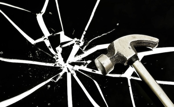 A hammer lies poised beside a radial pattern of broken glass shards on a black background, symbolizing resilience amidst chaos.